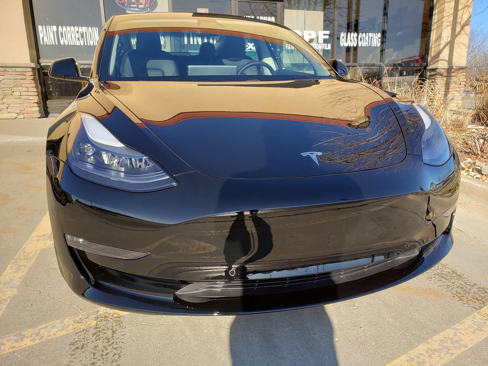The shop's storefront reflected in the black paint of a Tesla Model 3