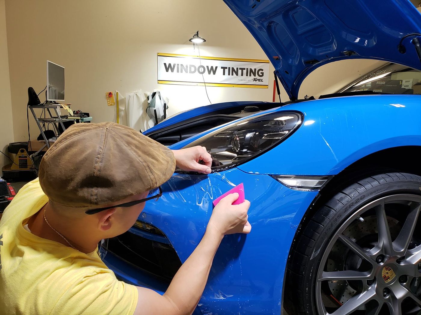 Squeegeeing a paint protection film edge at the headlight of a blue Porsche