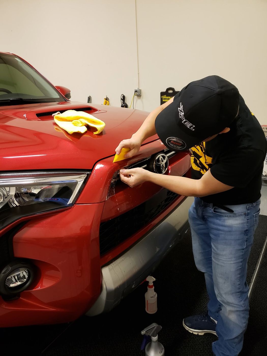 Vang Ge Lee wrapping paint protection film around the grille of a red Toyota 4Runner